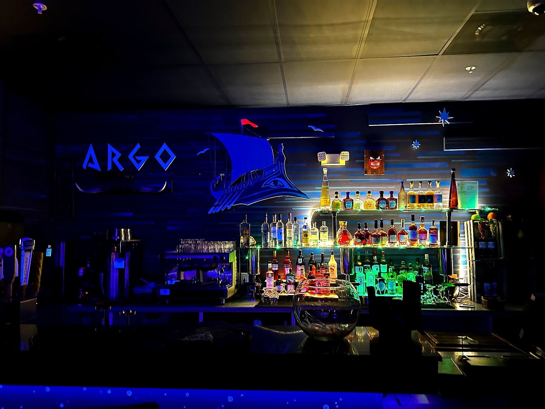 The neon blue Argo Greek-ship mural above the backlit full bar