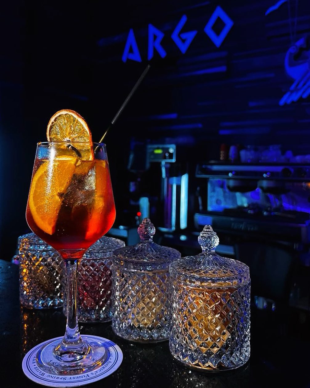 A signature spritz cocktail glowing under the neon ARGO sign